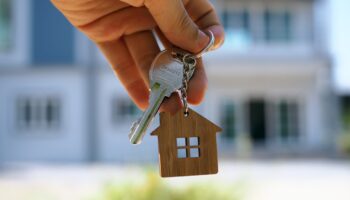 A hand holds a key on a keyring with a charm of a wooden house.