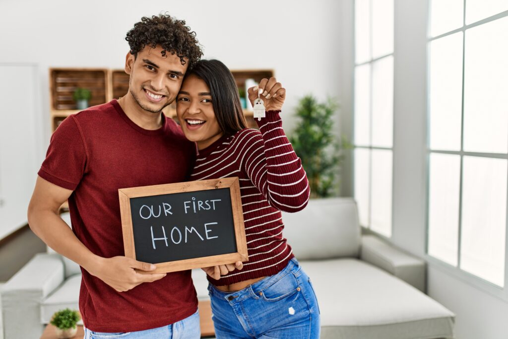 Young couple in new home holding a sign that says our first home